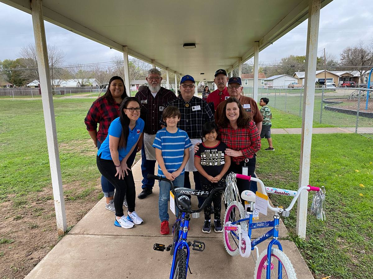 Lodge members and school staff pose under a covered walkway with two students and their new bicycles