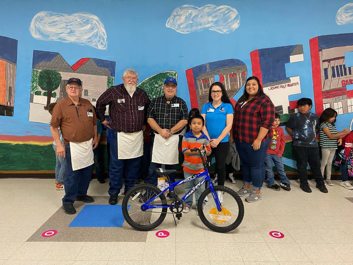 A young student stands behind his new blue bicycle with three lodge members and two school staff members