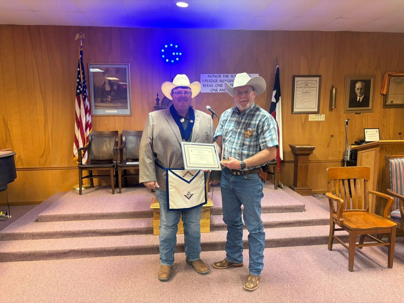 Sheriff Mike Lane and a lodge member in a white apron hold the Community Builder Award certificate in the lodge room