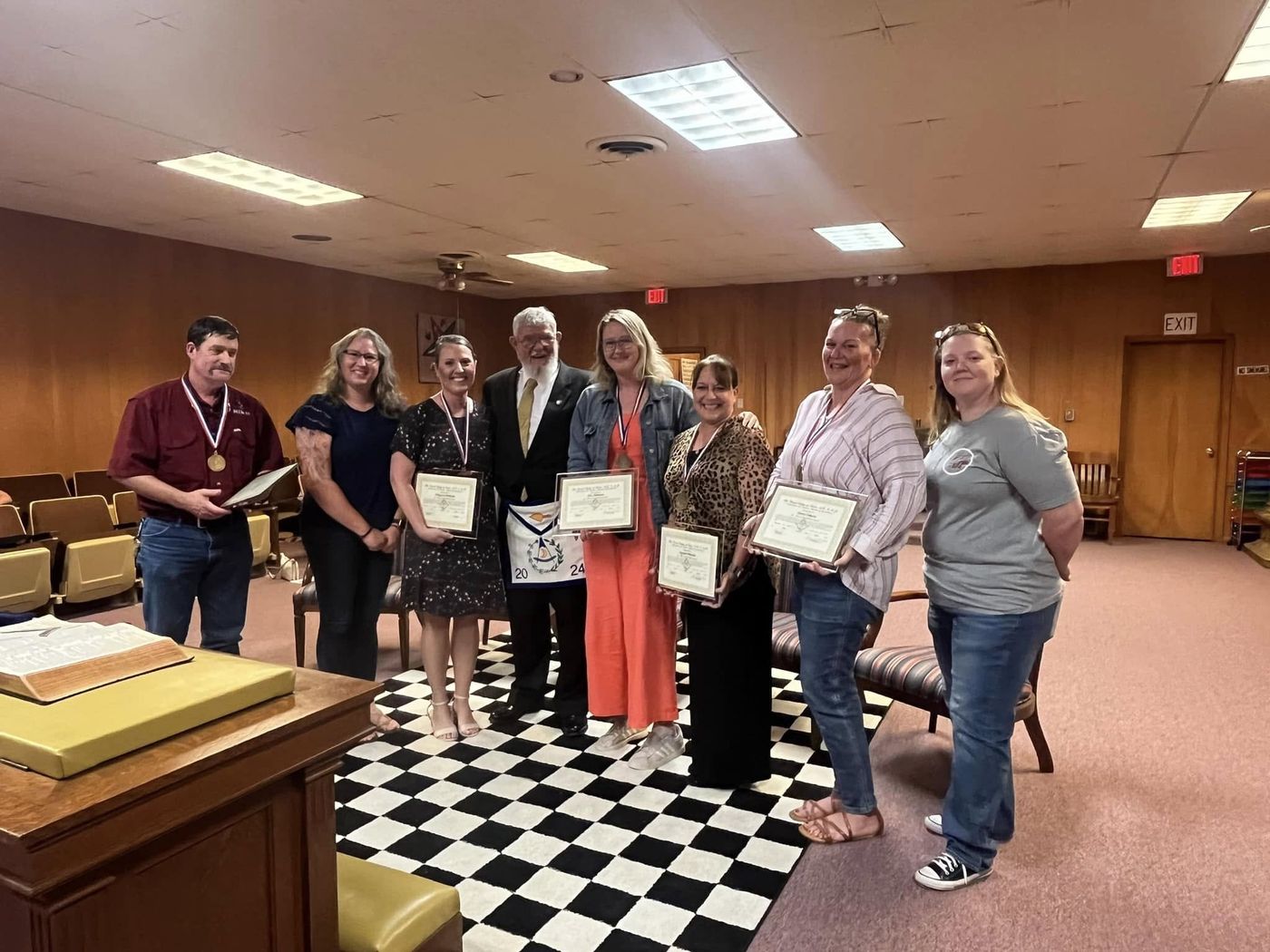 Lockhart ISD staff members hold Lamar Award certificates and medals beside a lodge officer in the lodge room